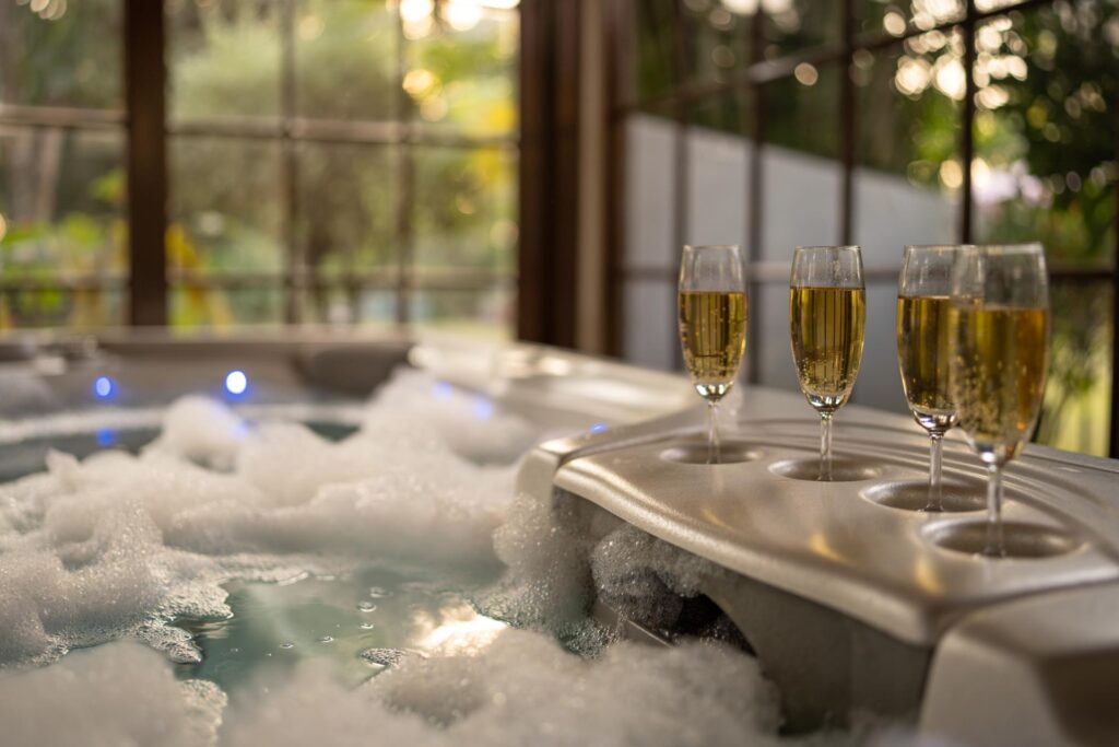 Glasses lined up on the rim of the bubbling jacuzzi, the garden beyond the windows